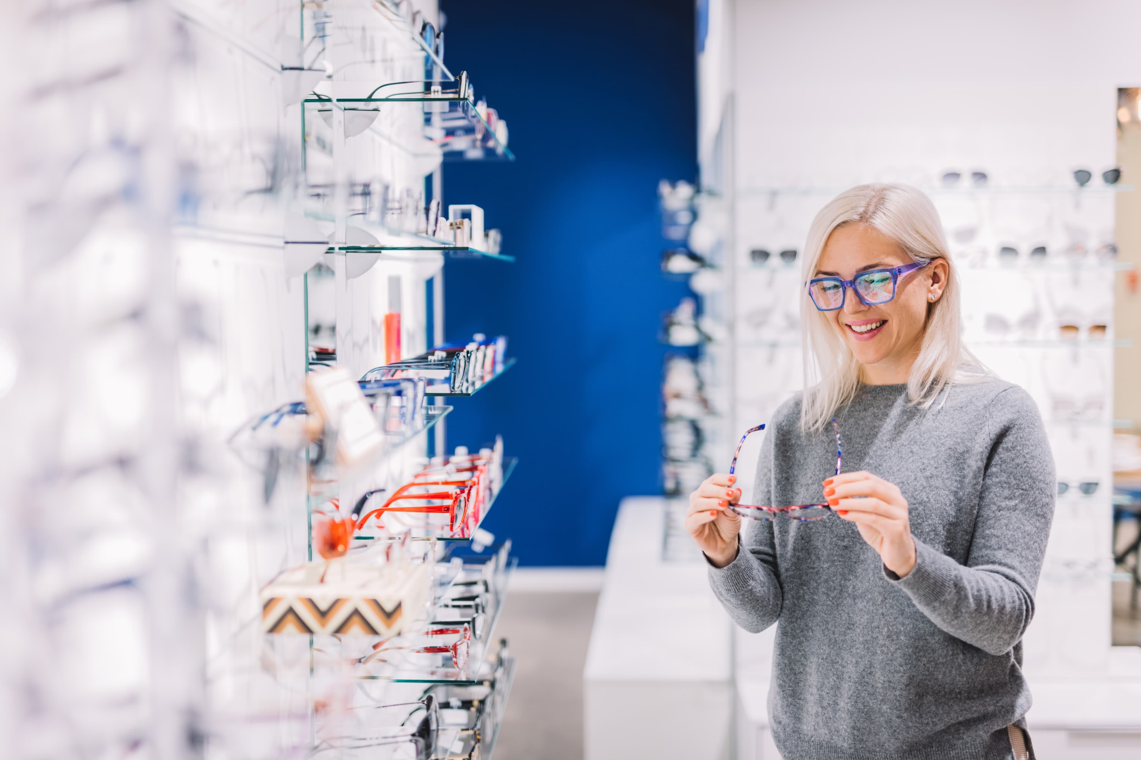 Woman with blue glasses holding eyeglasses in an optical store
